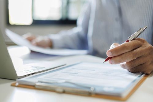 © Montri - stock.adobe.com Foto: Person mit Dokumenten und Laptop